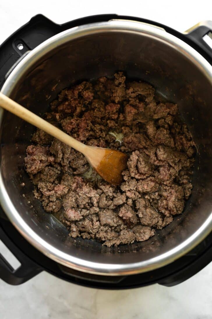 Browned ground beef in an Instant Pot with a wooden spoon.