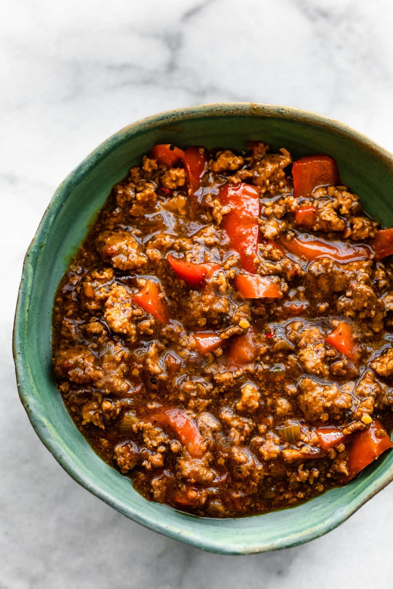 Overhead bowl of saucy beef bulgogi with red peppers in a blue ceramic bowl.