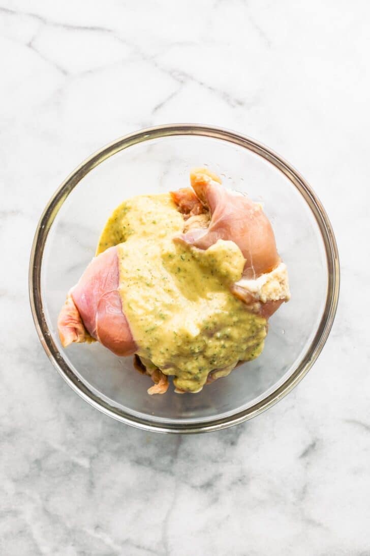 Lemon sage marinade over chicken thighs in a glass bowl.