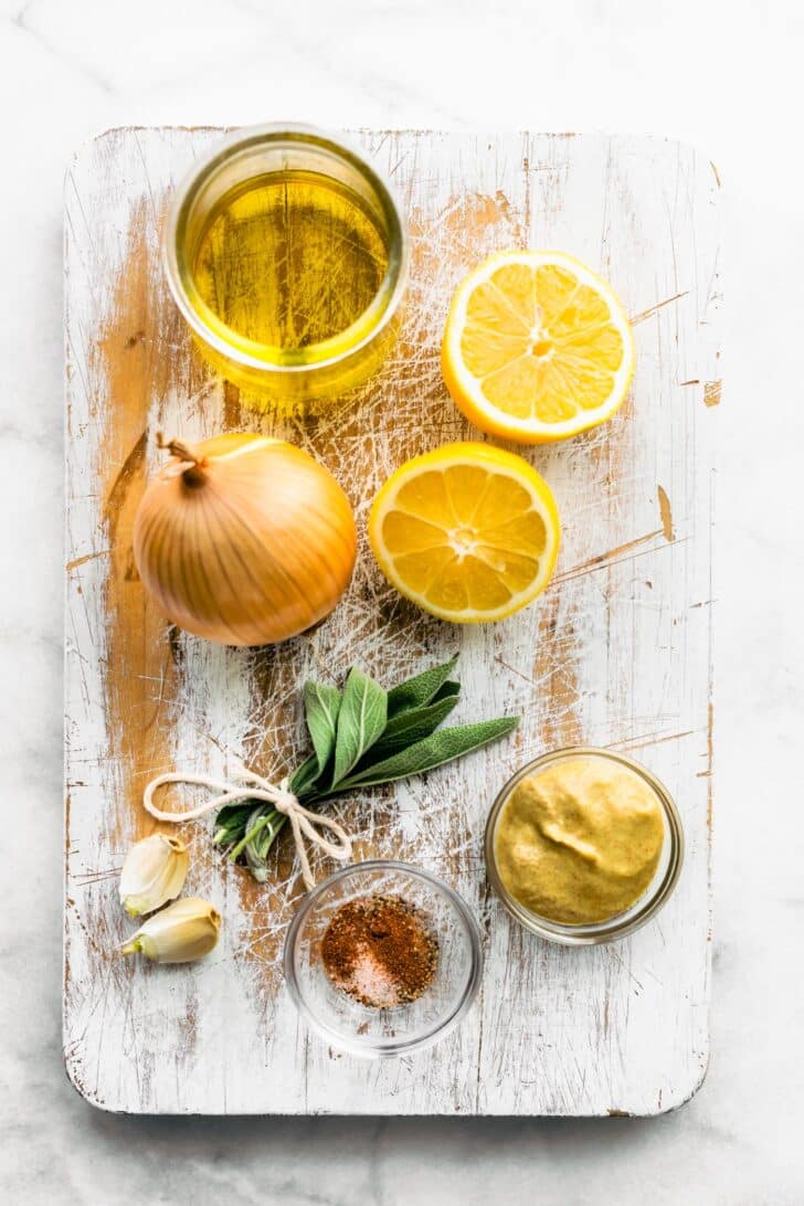 Ingredients for lemon sage chicken on a white wooden cutting board.