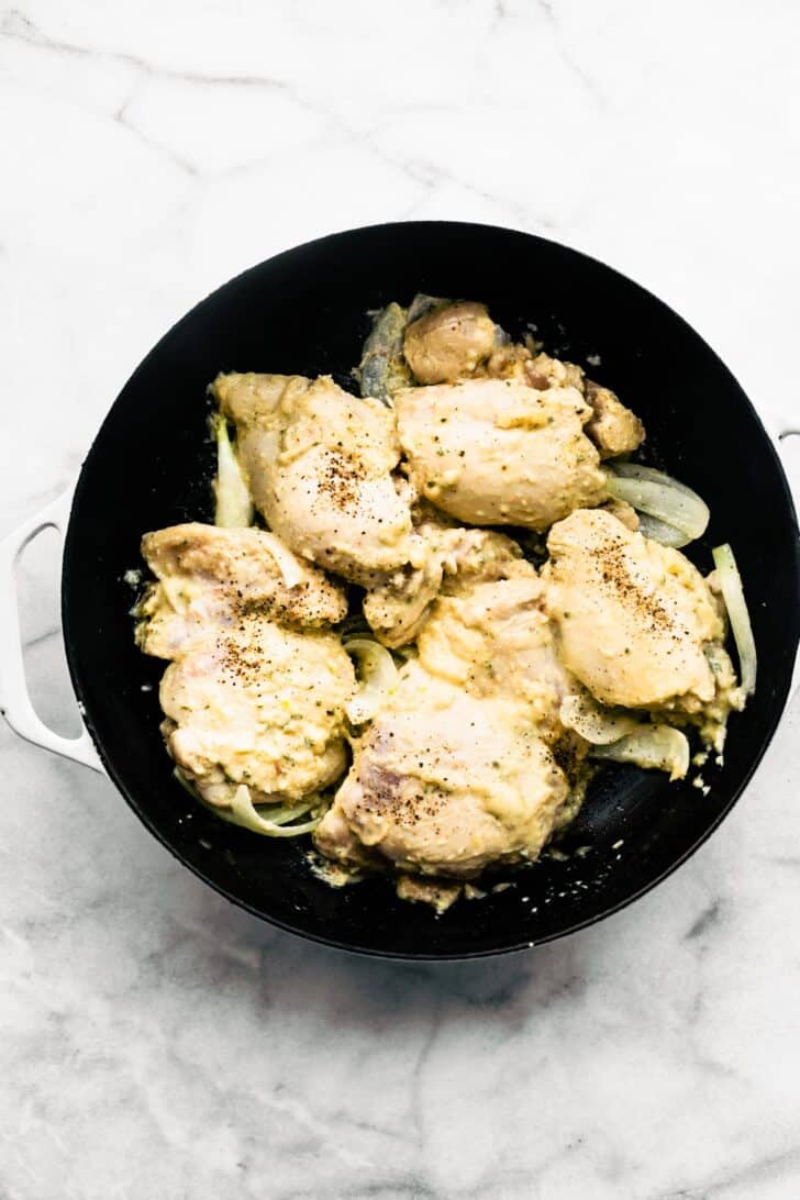 Chicken thighs with onion slices browning in cast iron sillet.
