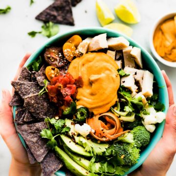 Two hands holding turquoise bowl filled with leftover turkey nachos salad bowl.