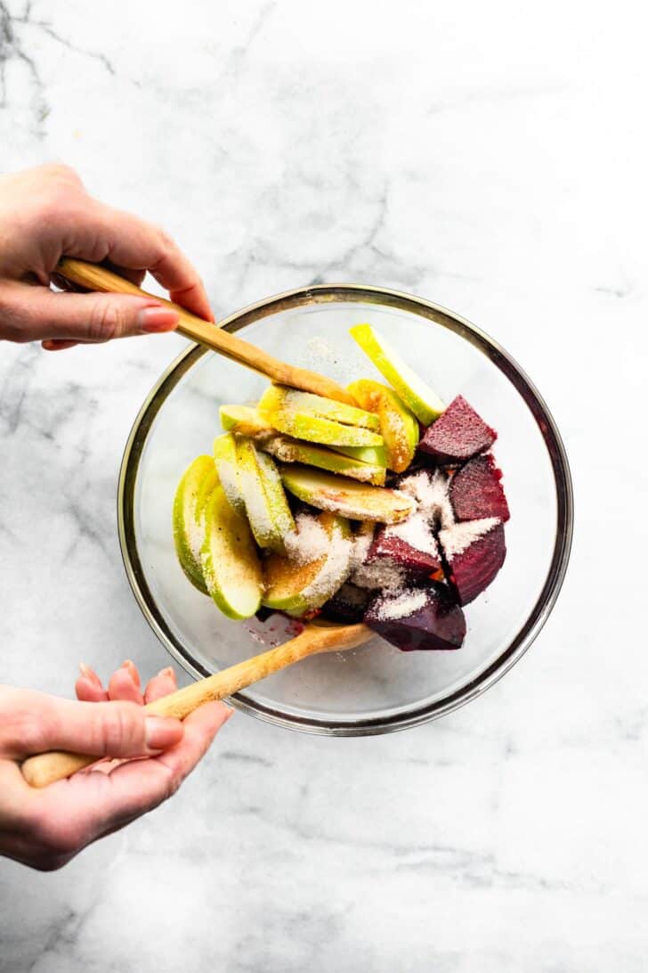 womens hands tossing chopped apple and beets with seasonings in a clear bowl
