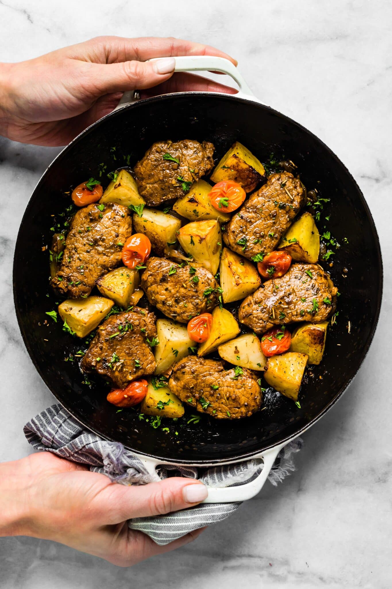 Overhead photo of a woman holding a pan of roasted pork and veggies.