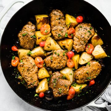 Overhead photo of cooked Mediterranean pork medallions with potatoes and tomatoes.