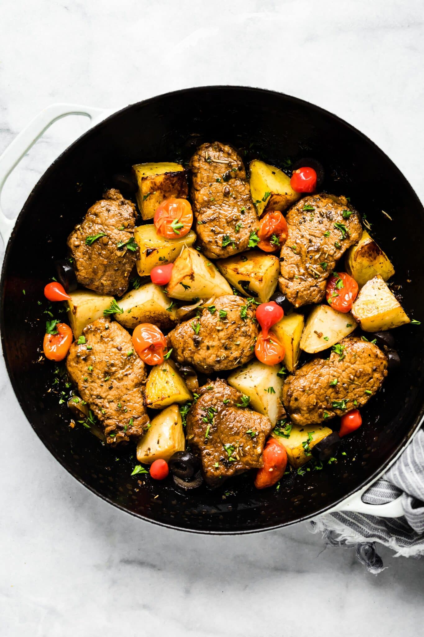 Overhead photo of cooked Mediterranean pork medallions with potatoes and tomatoes.