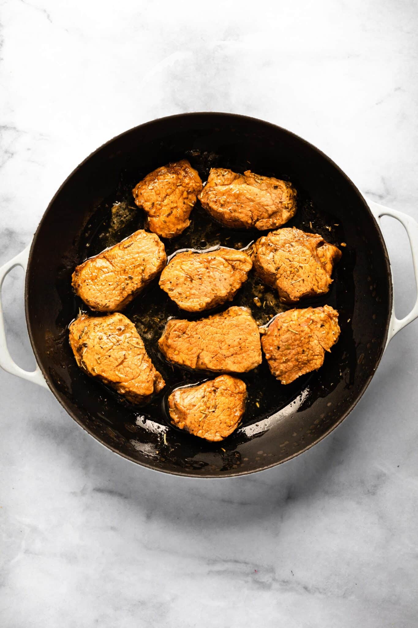 Marinated pork medallions in a cast iron skillet.