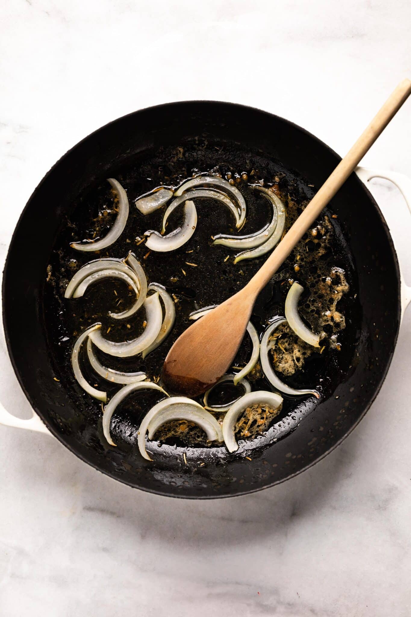 Sliced onions and oil in a cast iron pan with a wooden spoon.