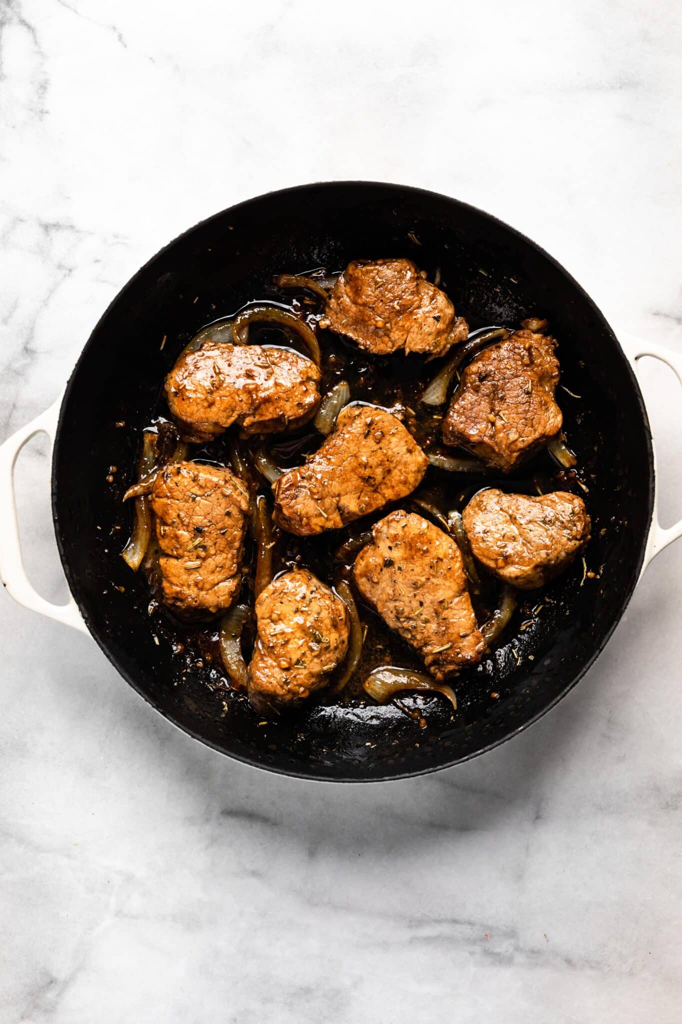 Seared pork medallions and sliced onions in a cast iron pan.