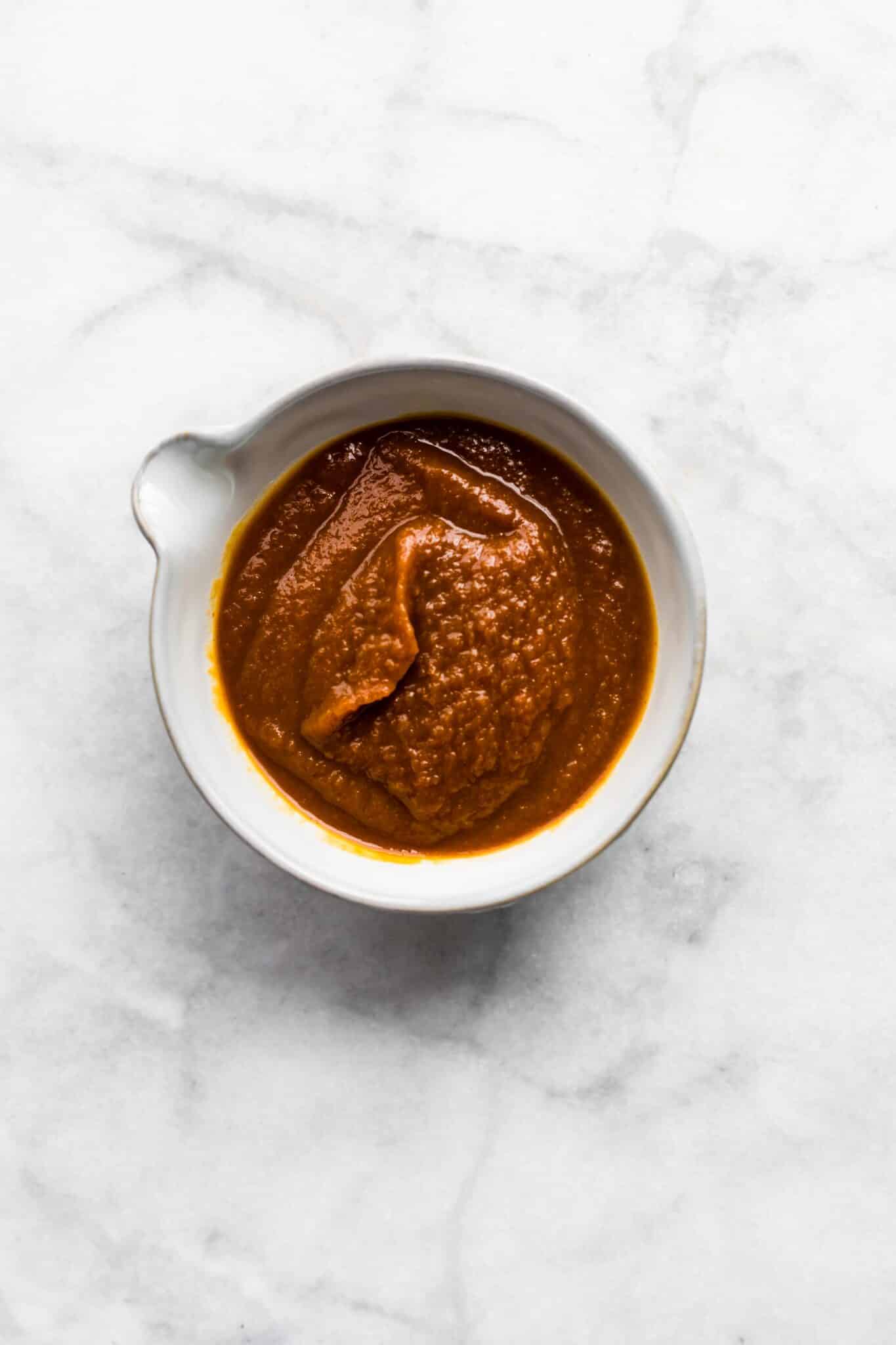 Homemade barbeque sauce in a white dish on a marble countertop.