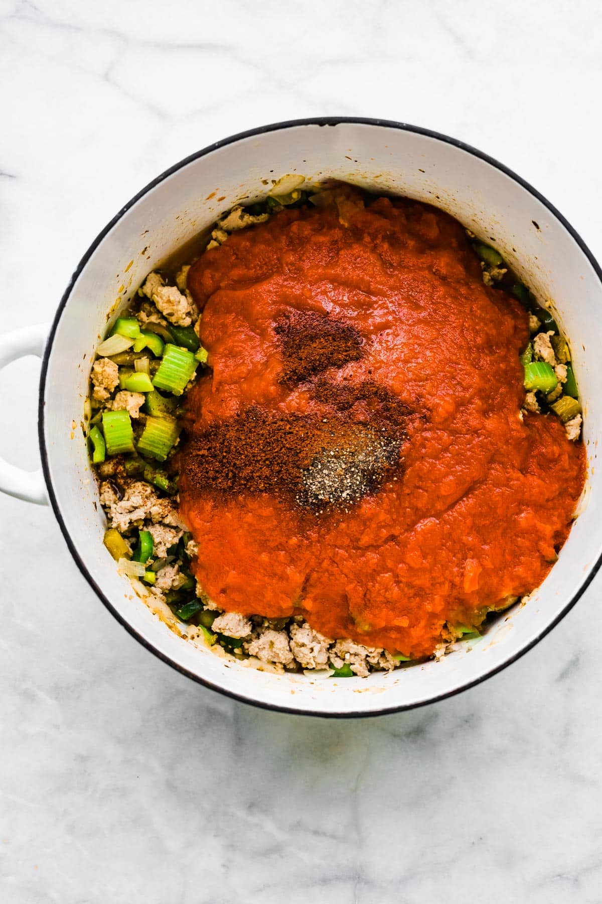 Overhead photo of crushed tomatoes and spices over cooked ground turkey and veggies.