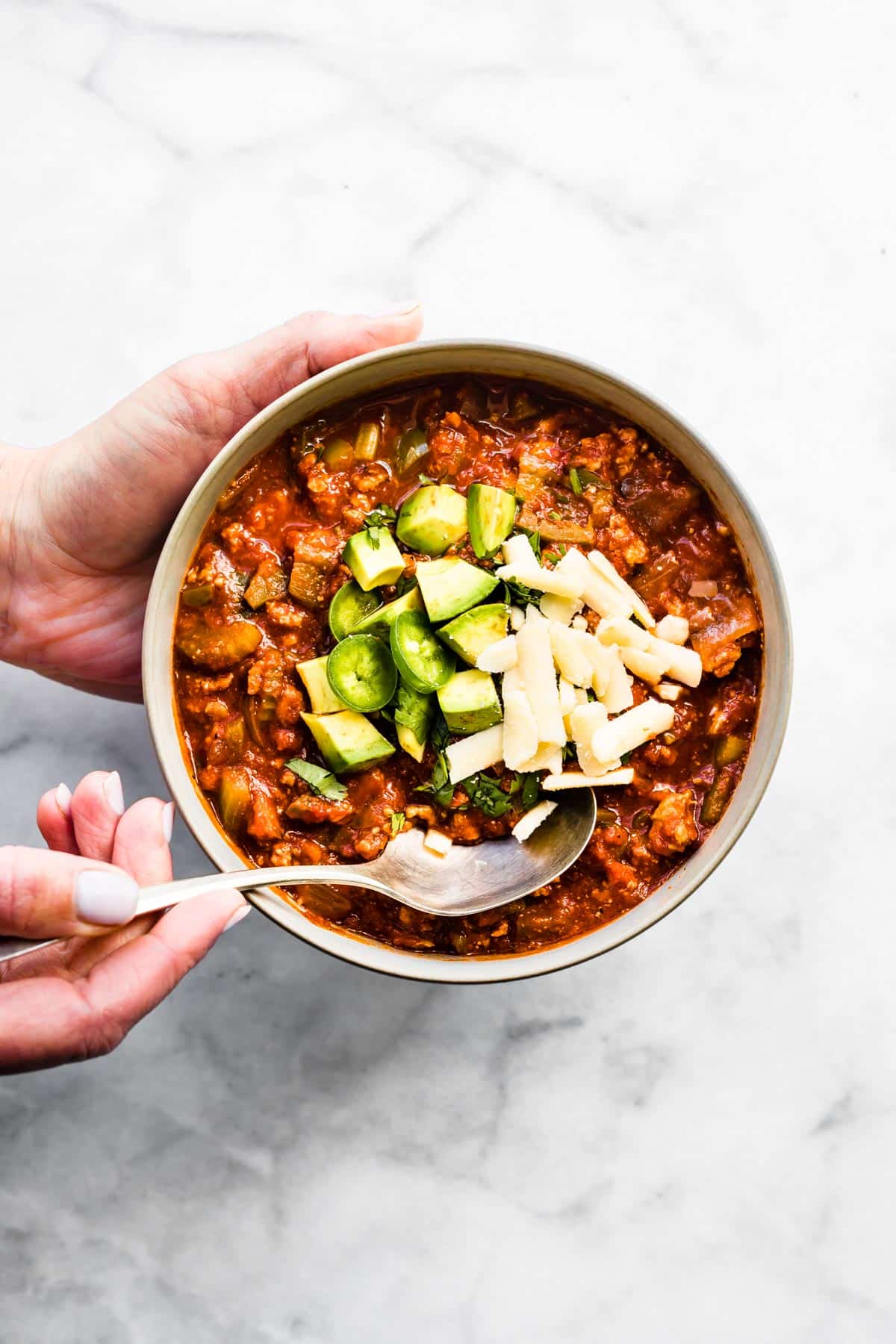 A woman holding a white bowl with beanless chili and dipping a spoon into it.