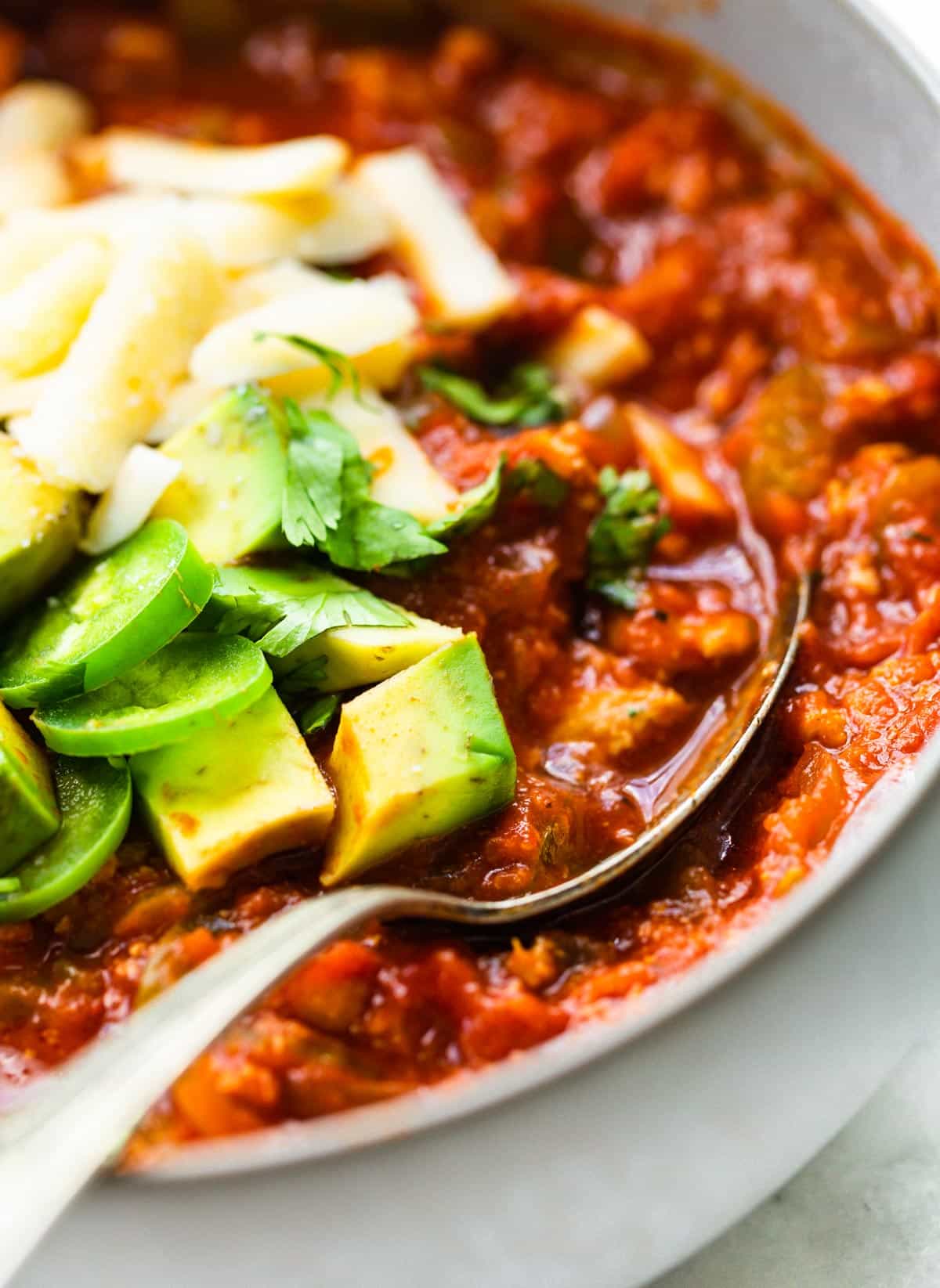 Up close photo of a spoon in a bowl of beanless chili topped with avocado.