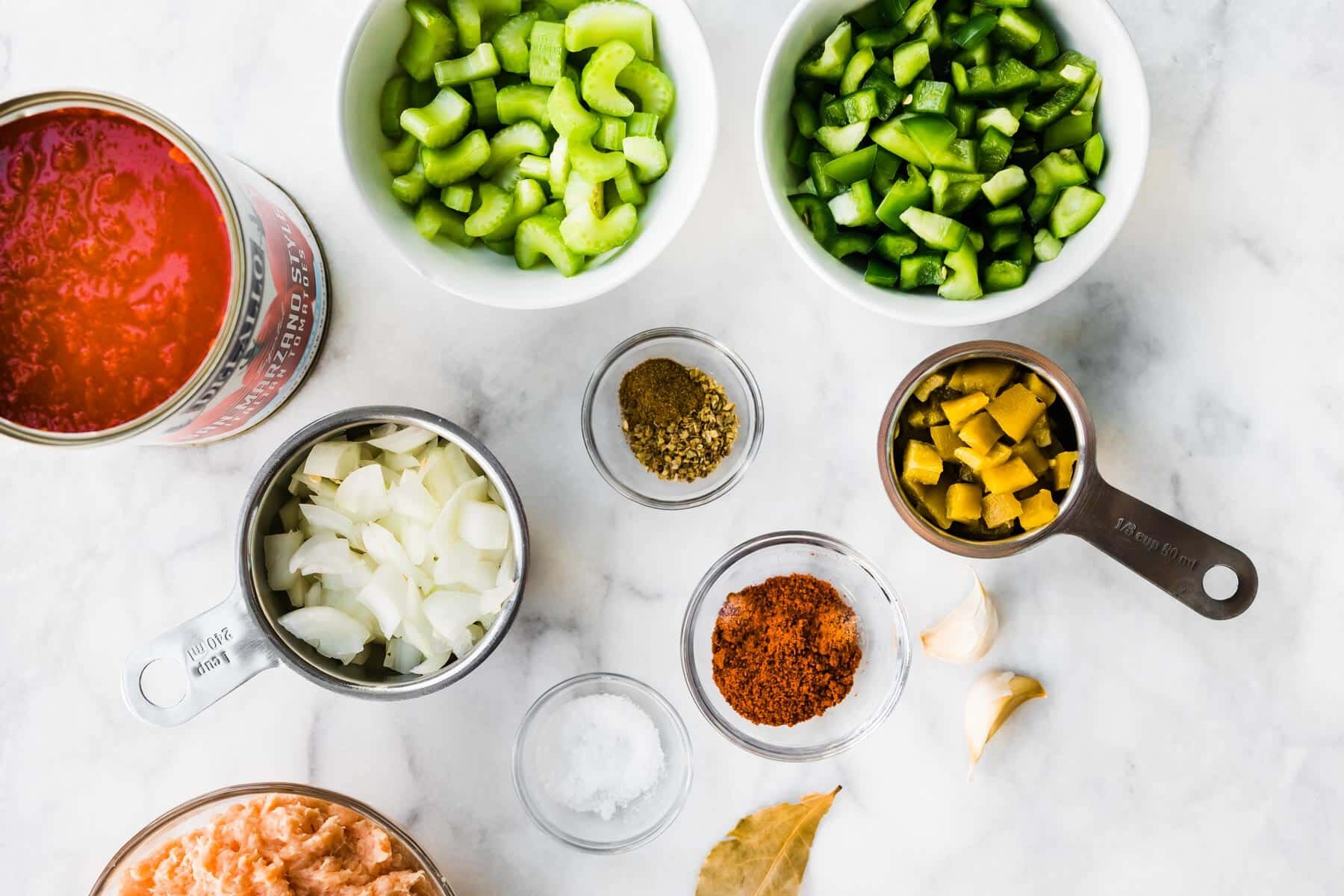 Canned tomatoes, jalapenos, onion, ground turkey and other ingredients for chili on a marble countertop.