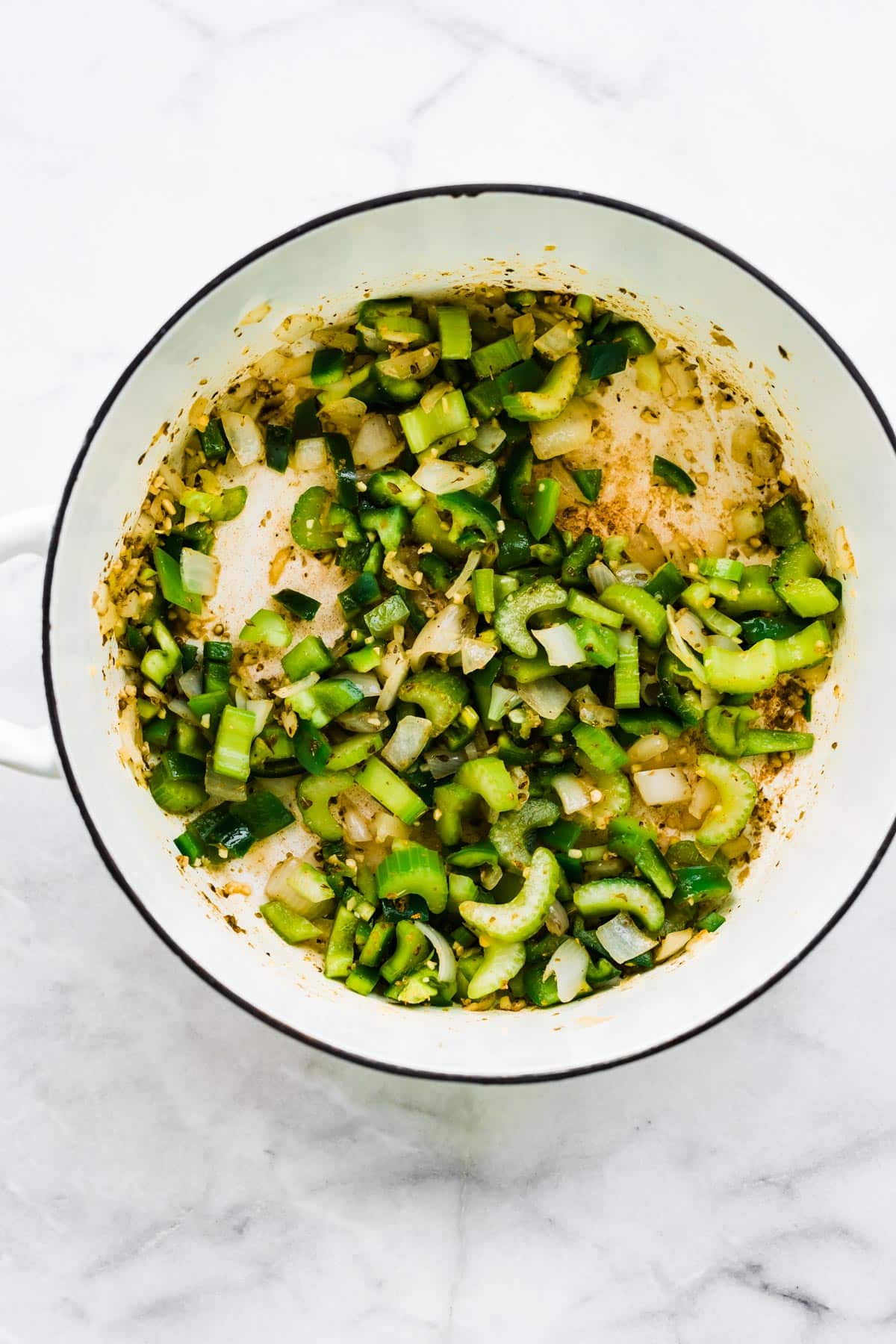 Overhead photo of a white pot with sauteed bell pepper, onion and celery.