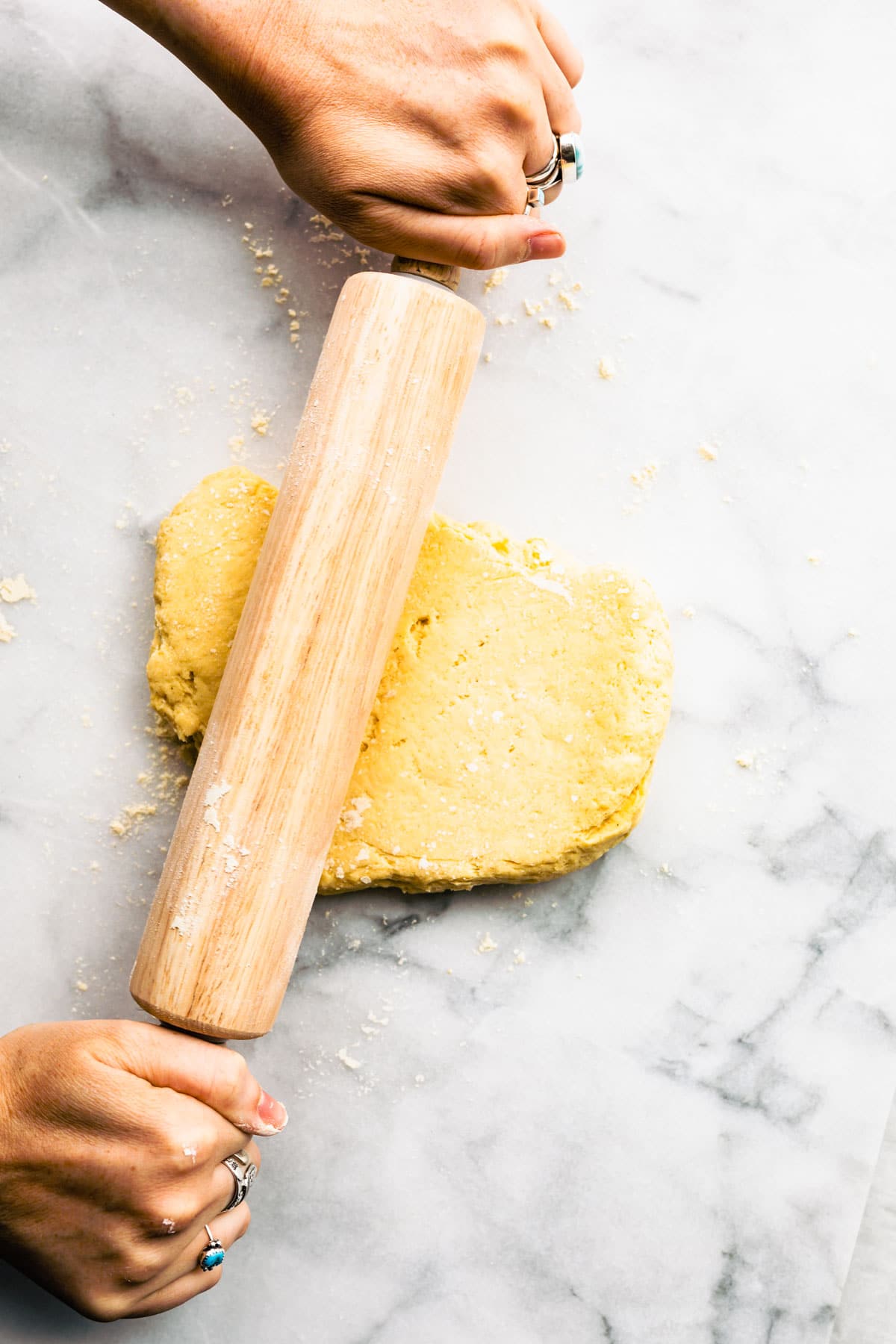 A woman's hands using a wooden rolling pin to roll out a ball of dough.
