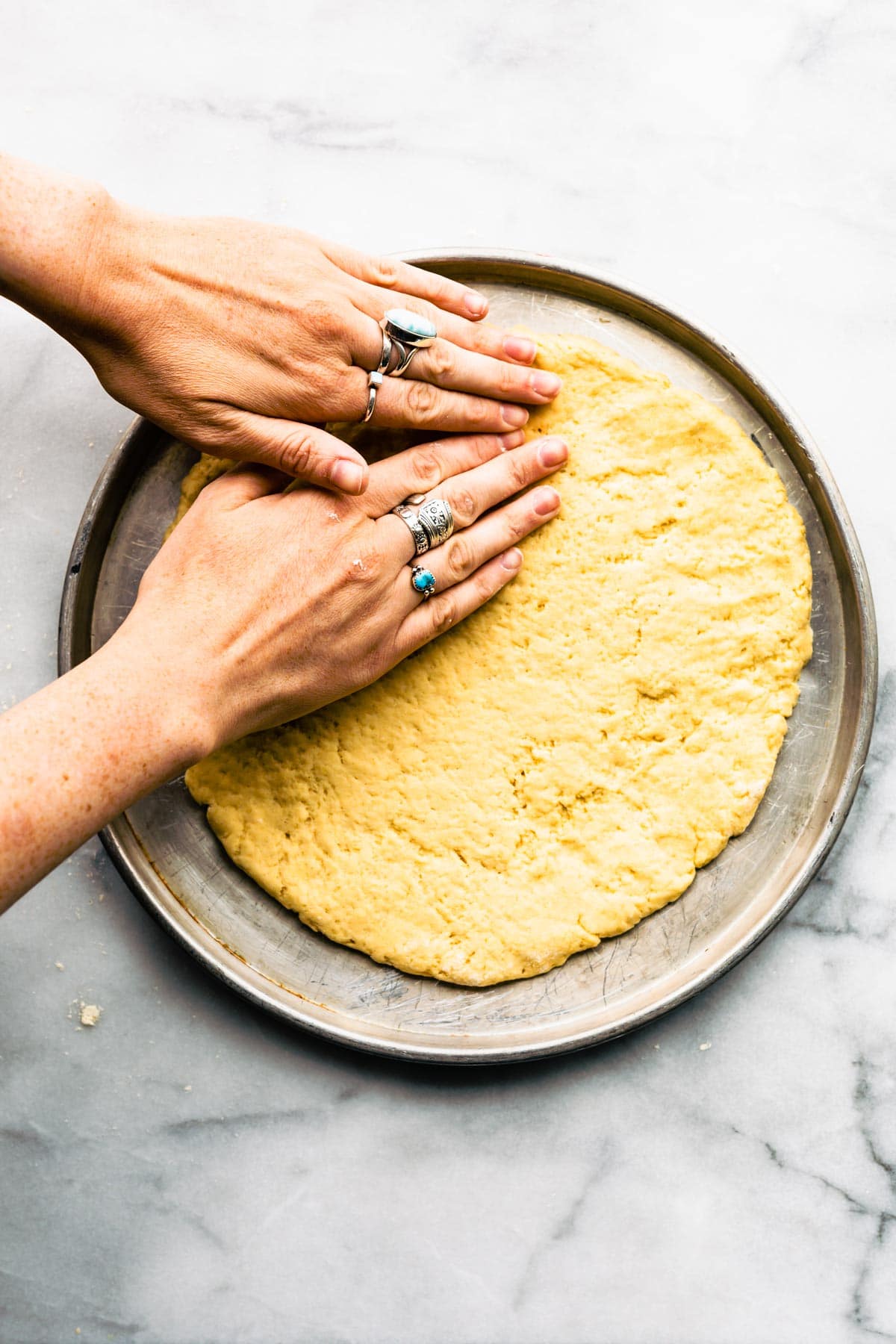 A woman's hands pressing no yeast pizza dough into shape on a metal pan.