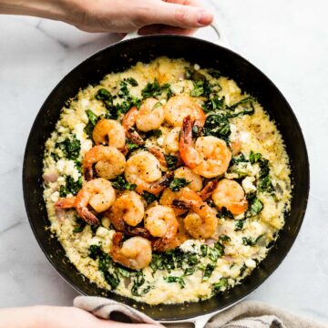 hero shot: woman's hands holding pan of cauliflower risotto shrimp skillet