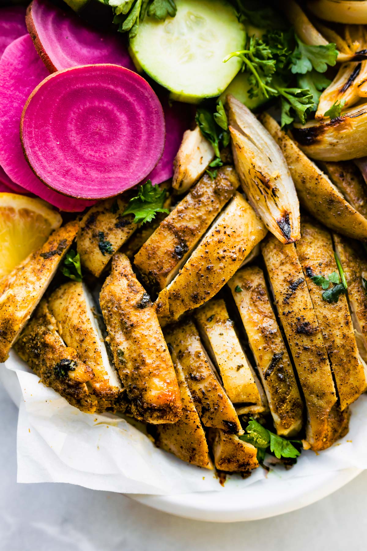 Overhead closeup of oven roasted slices of boneless skinless chicken thighs with pink pickles.