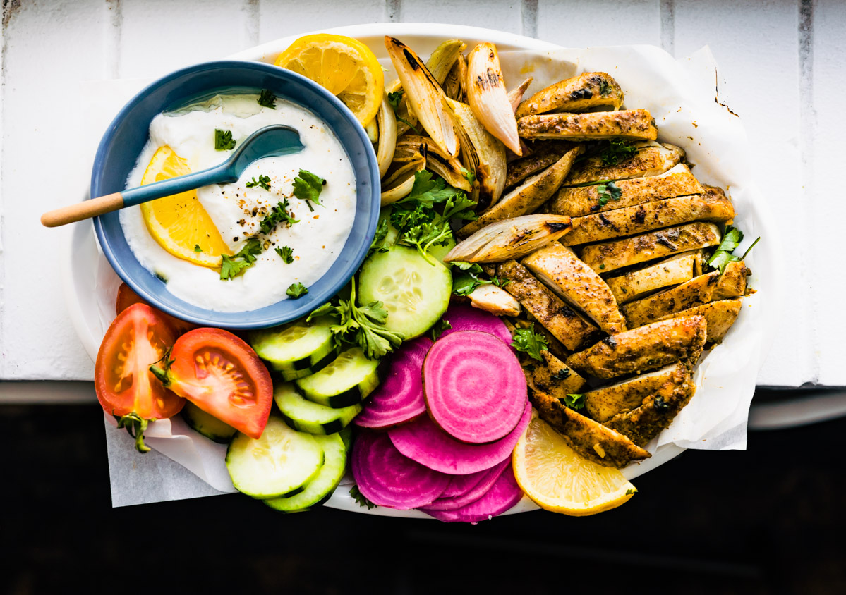 Overhead photo of oven roasted chicken shawarma on a platter with vegetables and shawarma sauce.