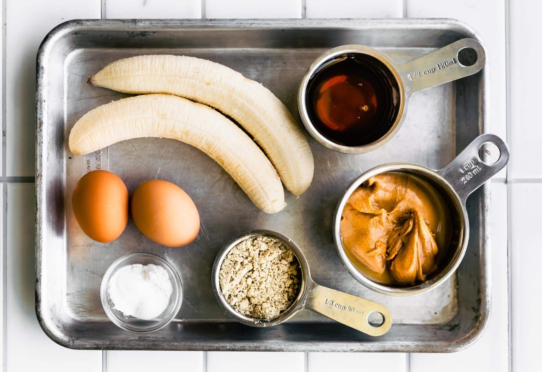 Peanut butter, bananas, maple syrup and eggs on a metal sheet pan.