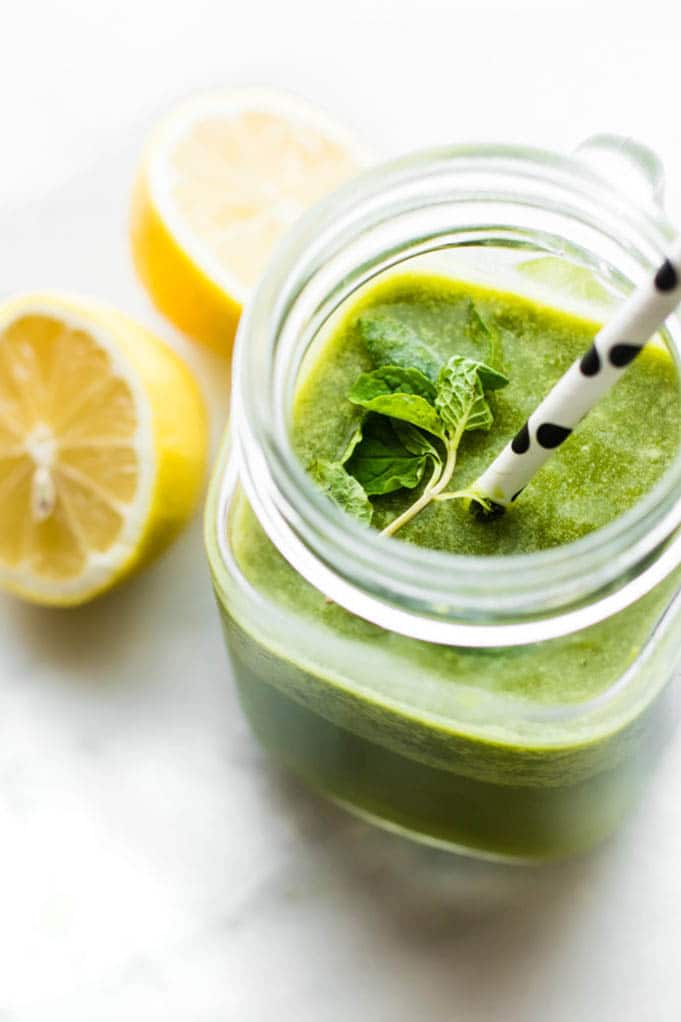 Bright green smoothie in mason jar cup topped with fresh mint