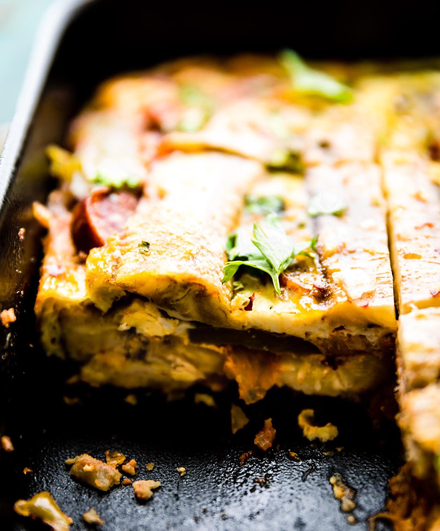 Close up side view of plantain lasagna in baking dish with slice removed to show layers.