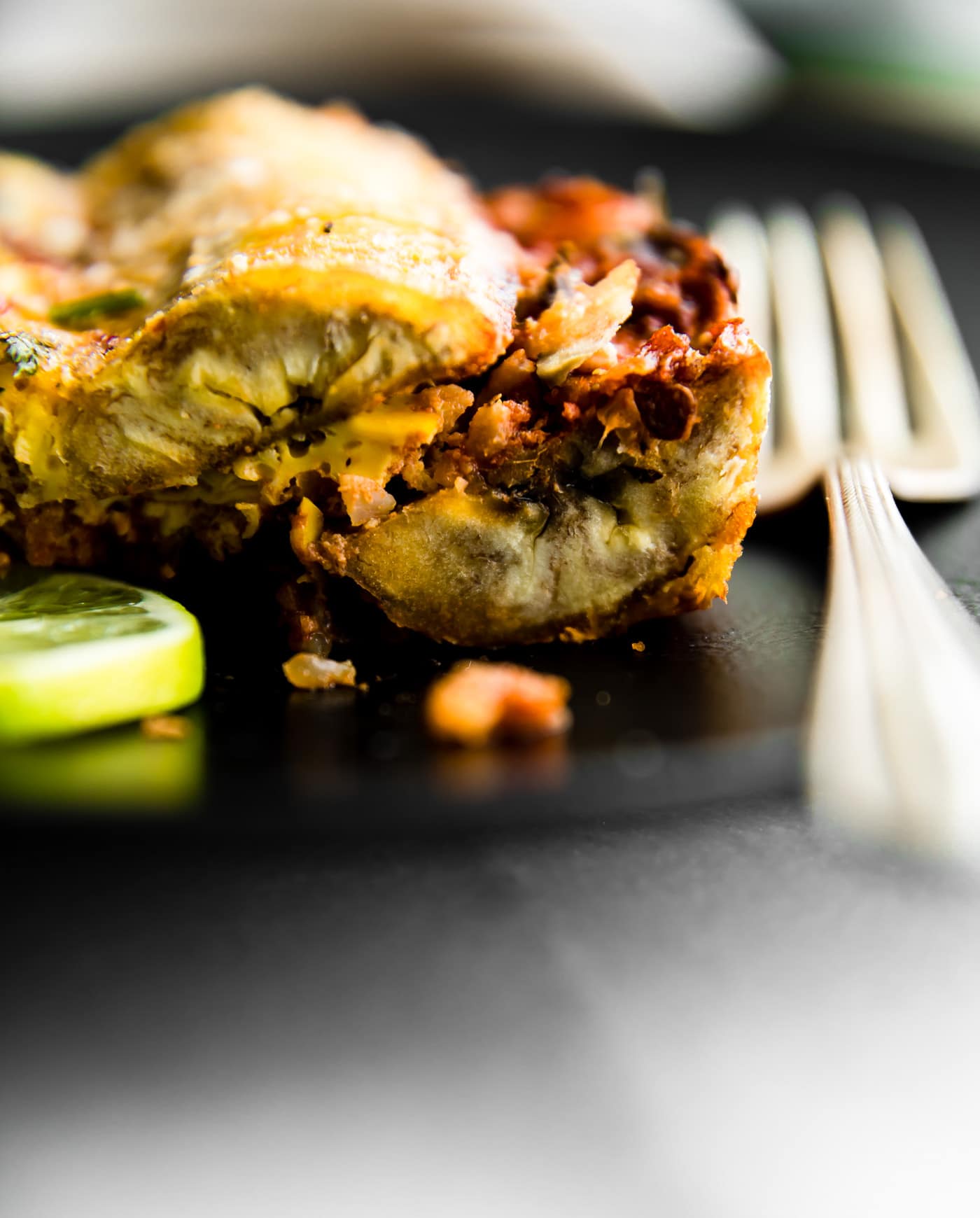 Close up side view slice of plantain breakfast lasagna on black plate