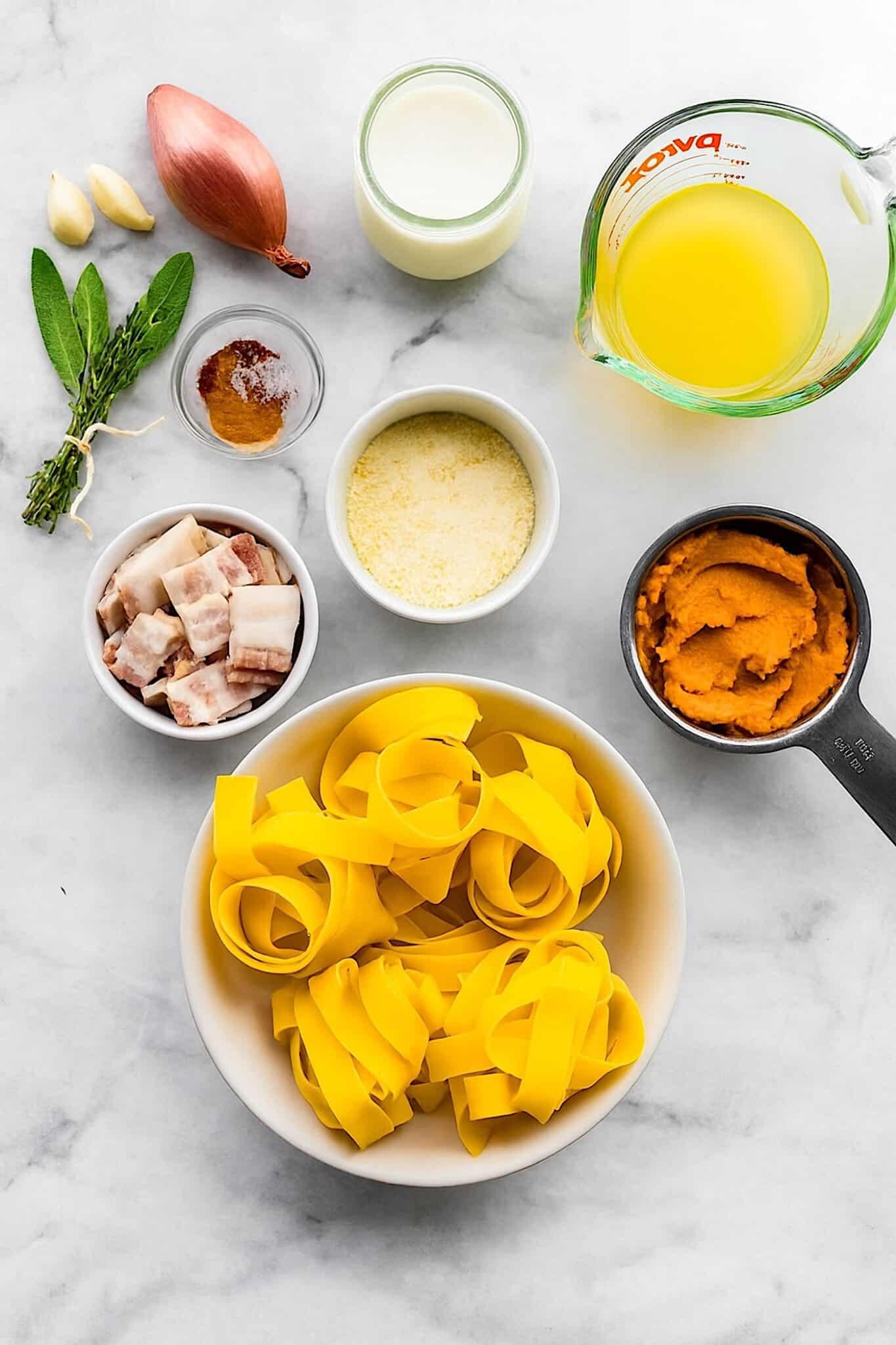 Pumpkin pasta ingredients flat lay with gluten-free pappardelle, pumpkin purée, parmesan, bacon, broth, garlic, shallot, herbs, and non-dairy cream