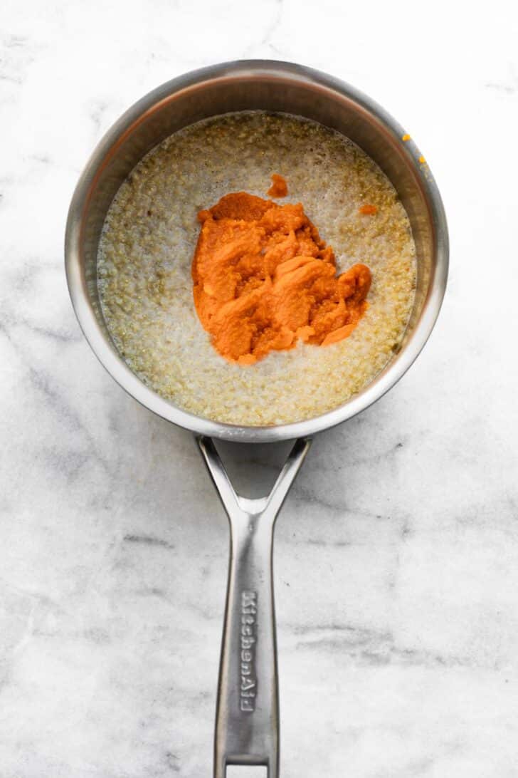 Pumpkin puree stirred into cooked quinoa with milk in saucepan.