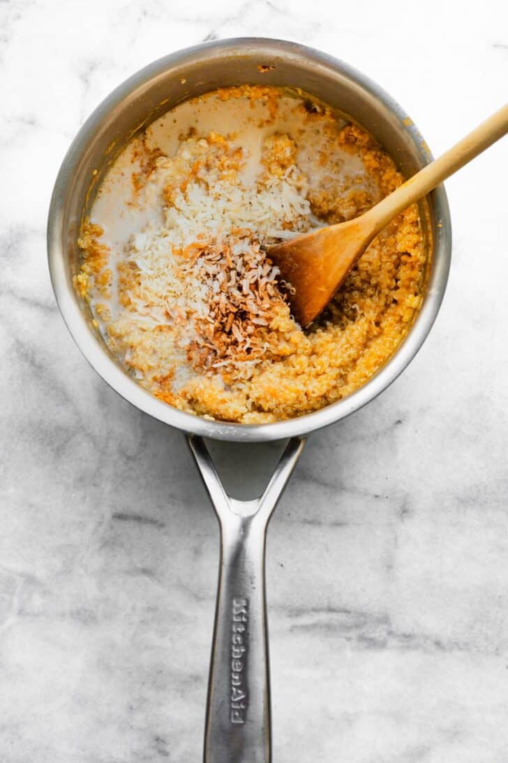Shredded coconut and cinnamon added to pumpkin quinoa in saucepan.