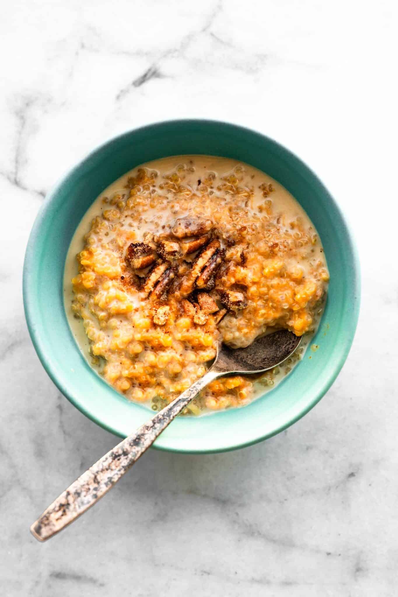 Creamy Pumpkin Quinoa breakfast porridge in blue bowl with silver spoon.
