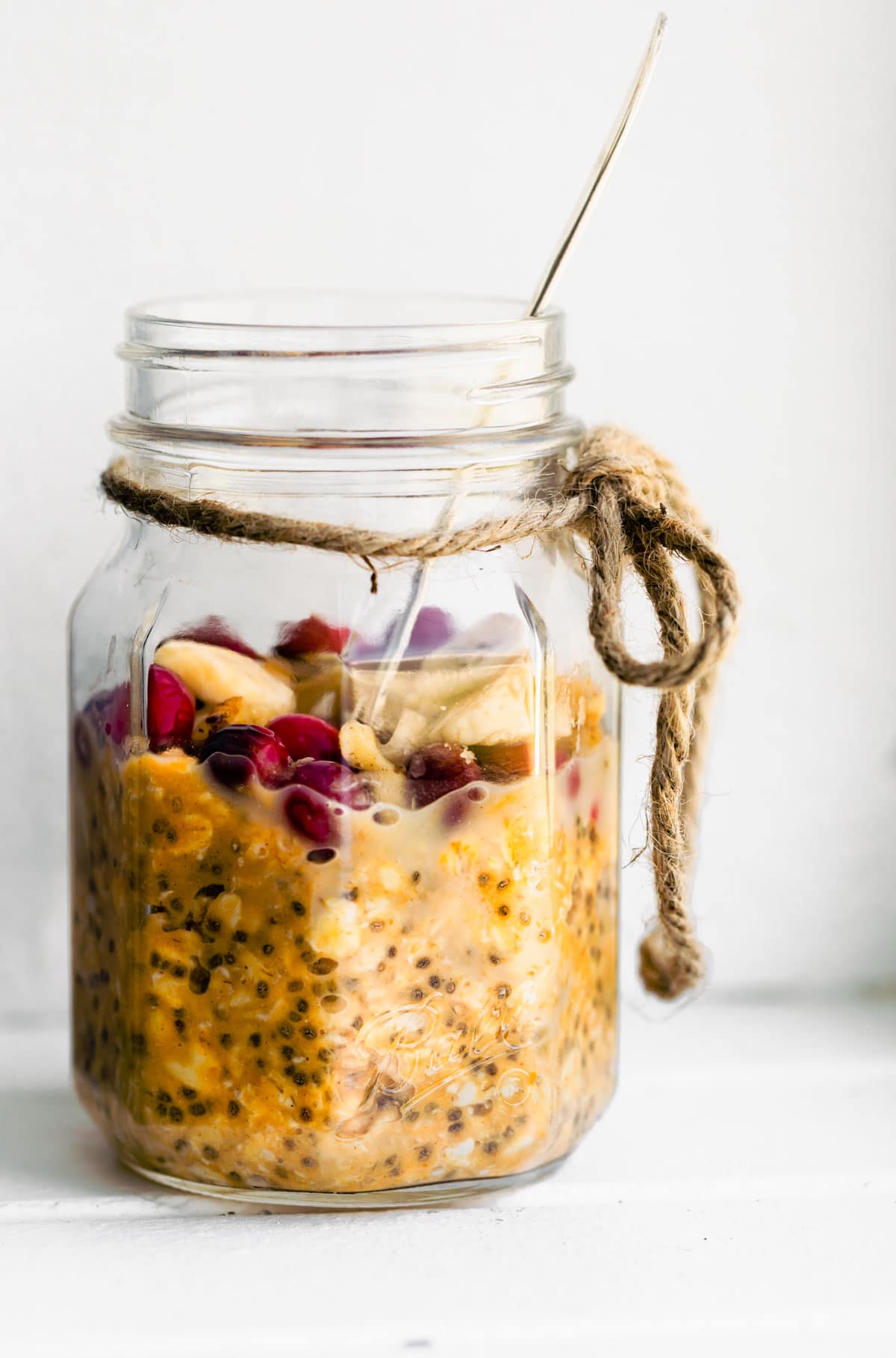 Easy Pumpkin Overnight Oats with cranberries, sliced bananas, and chopped nuts in a mason jar with a spoon in it.