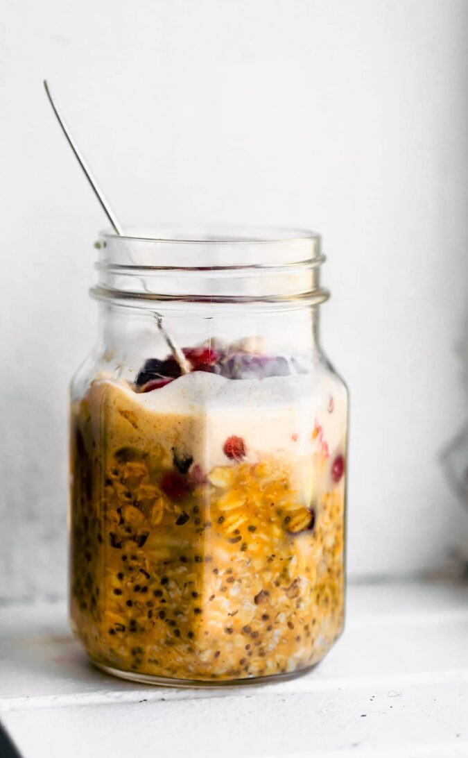 side view: jar of pumpkin overnight oats with vegan condensed milk on top. Spoon in the jar