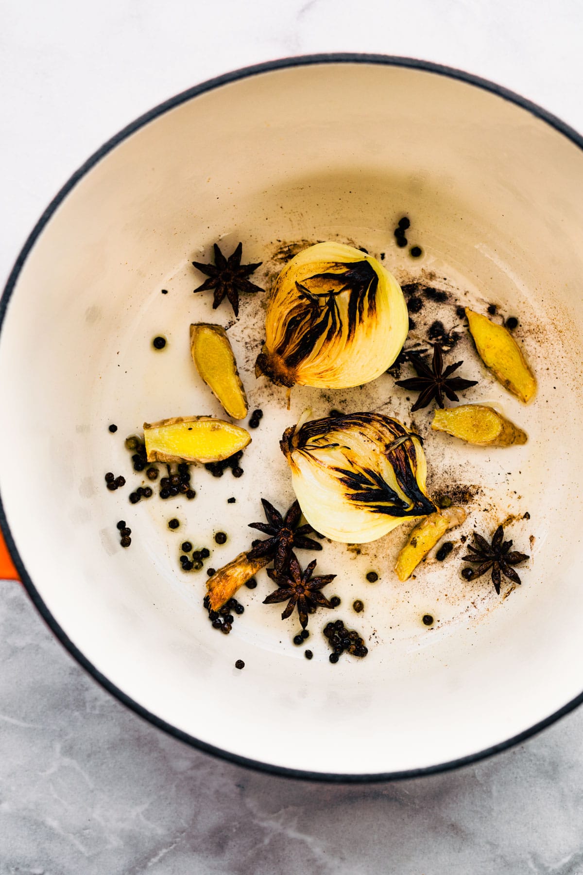 Overhead photo of sauteed onion halves, star anise and fresh ginger in a pot.