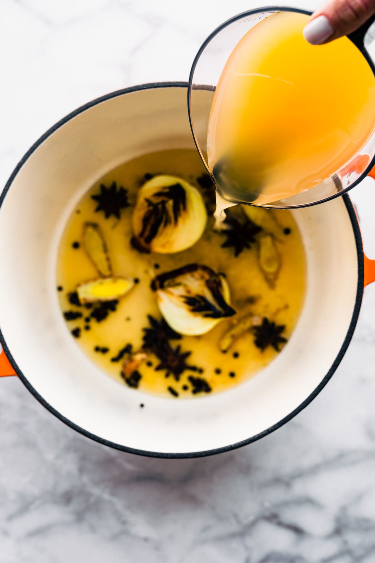 Pouring chicken stock into a saucepan of sauteed onion and star anise.