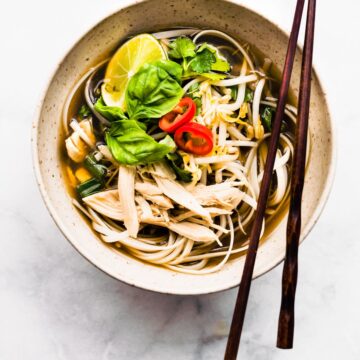 Overhead photo of chopsticks on a bowl of chicken pho ga with rice noodles.