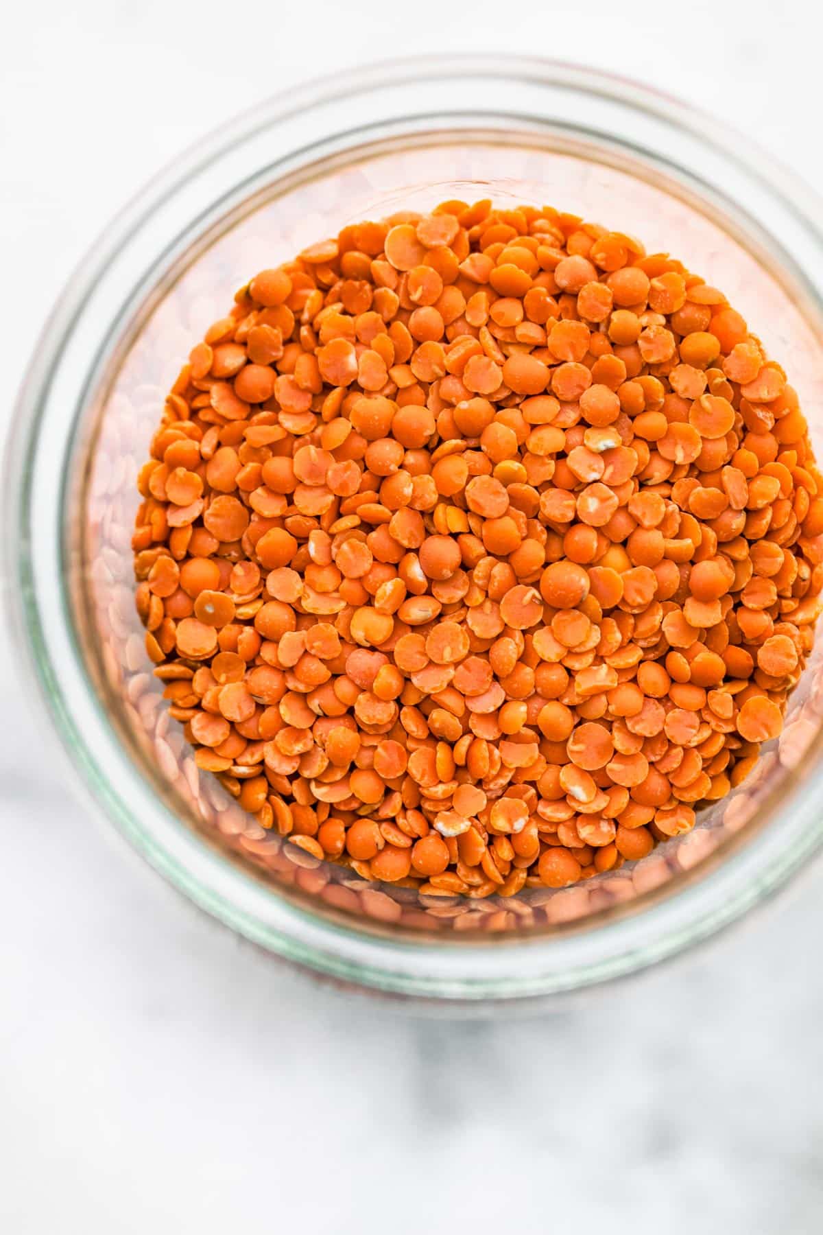An overhead shot of a glass jar full of red-ish orange Lentils.