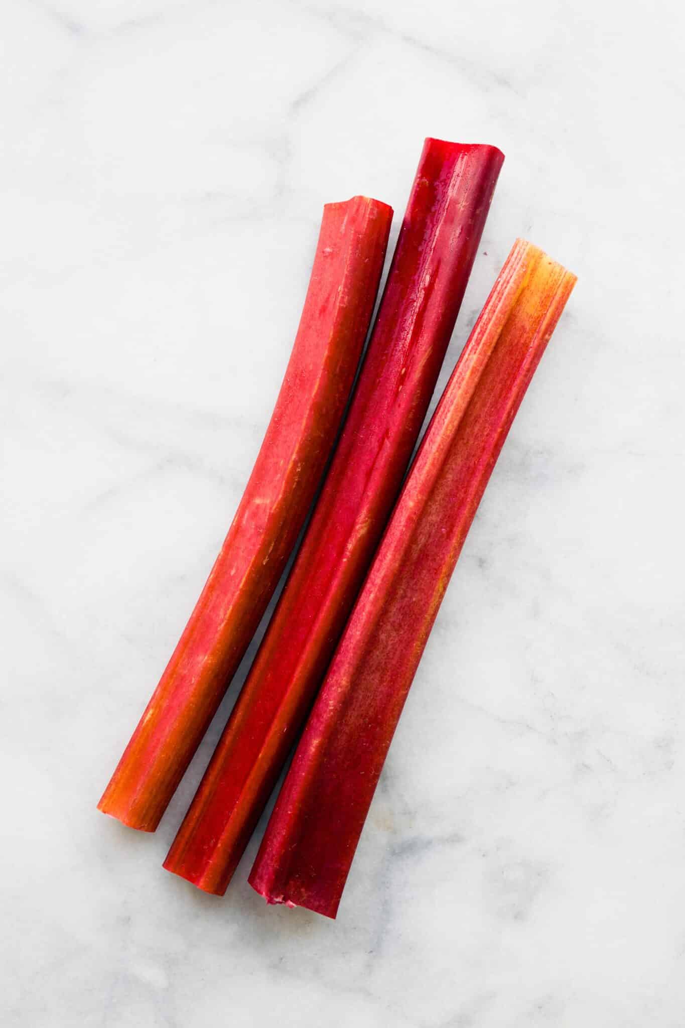 Three stalks of cut rhubarb on a white marble countertop.