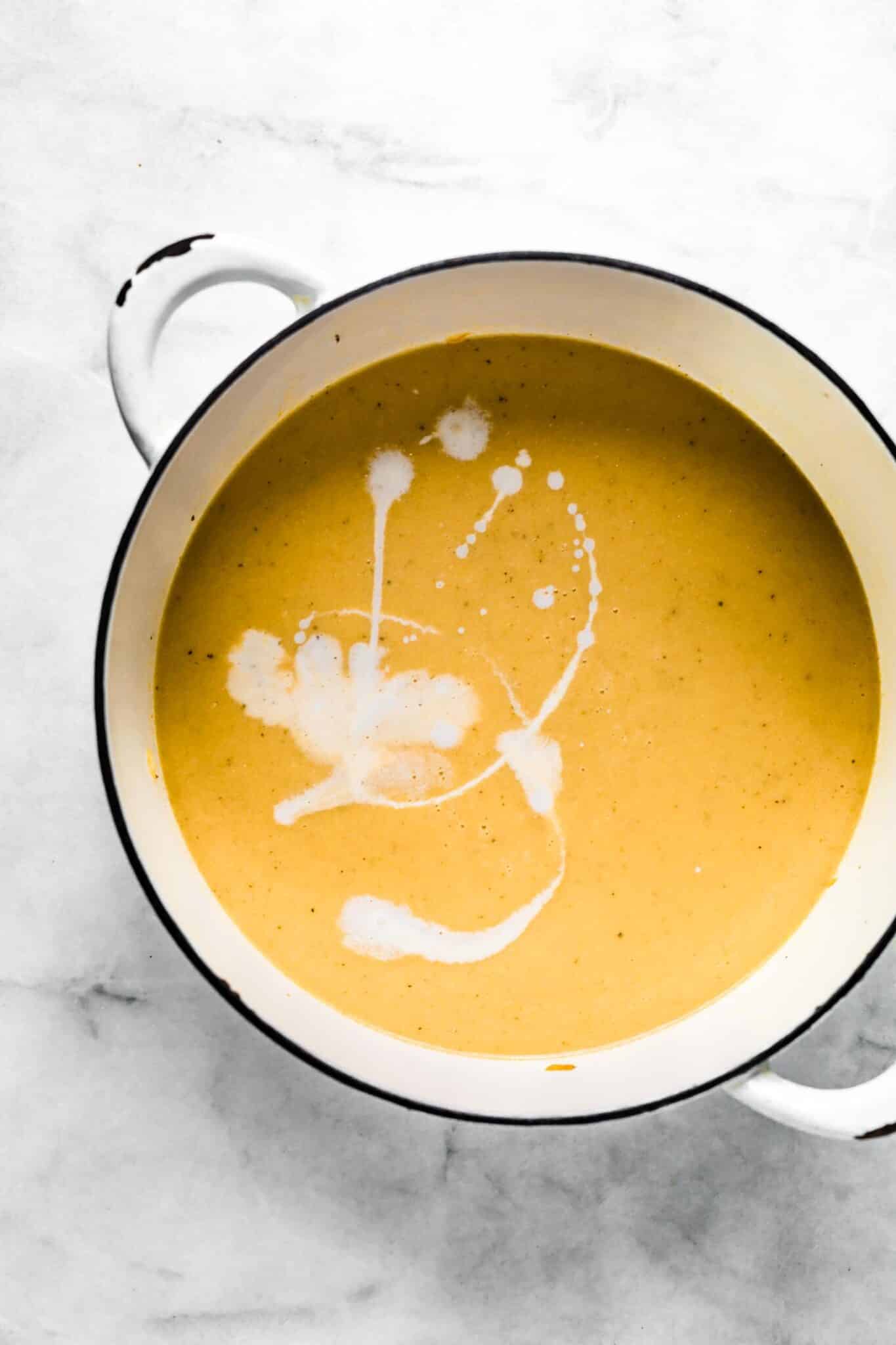 Coconut milk ready to be stirred into roasted cauliflower soup in a white pot.