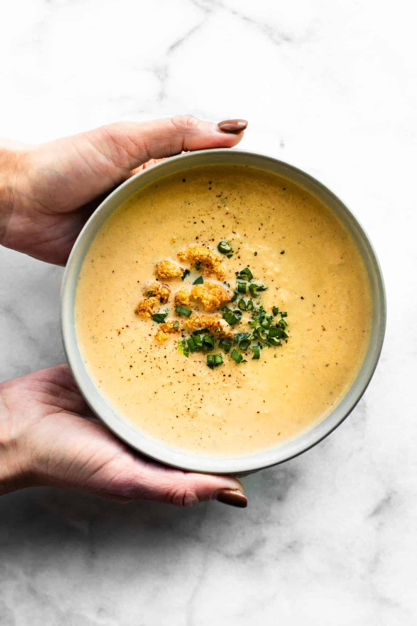 Overhead photo of a woman's hands holding a bowl of roasted cauliflower soup.