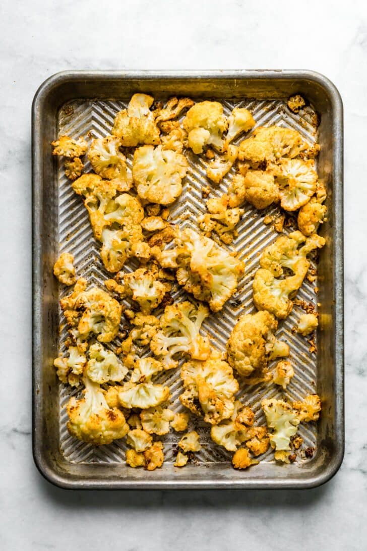 Overhead photo of roasted cauliflower florets on a vintage sheet pan.