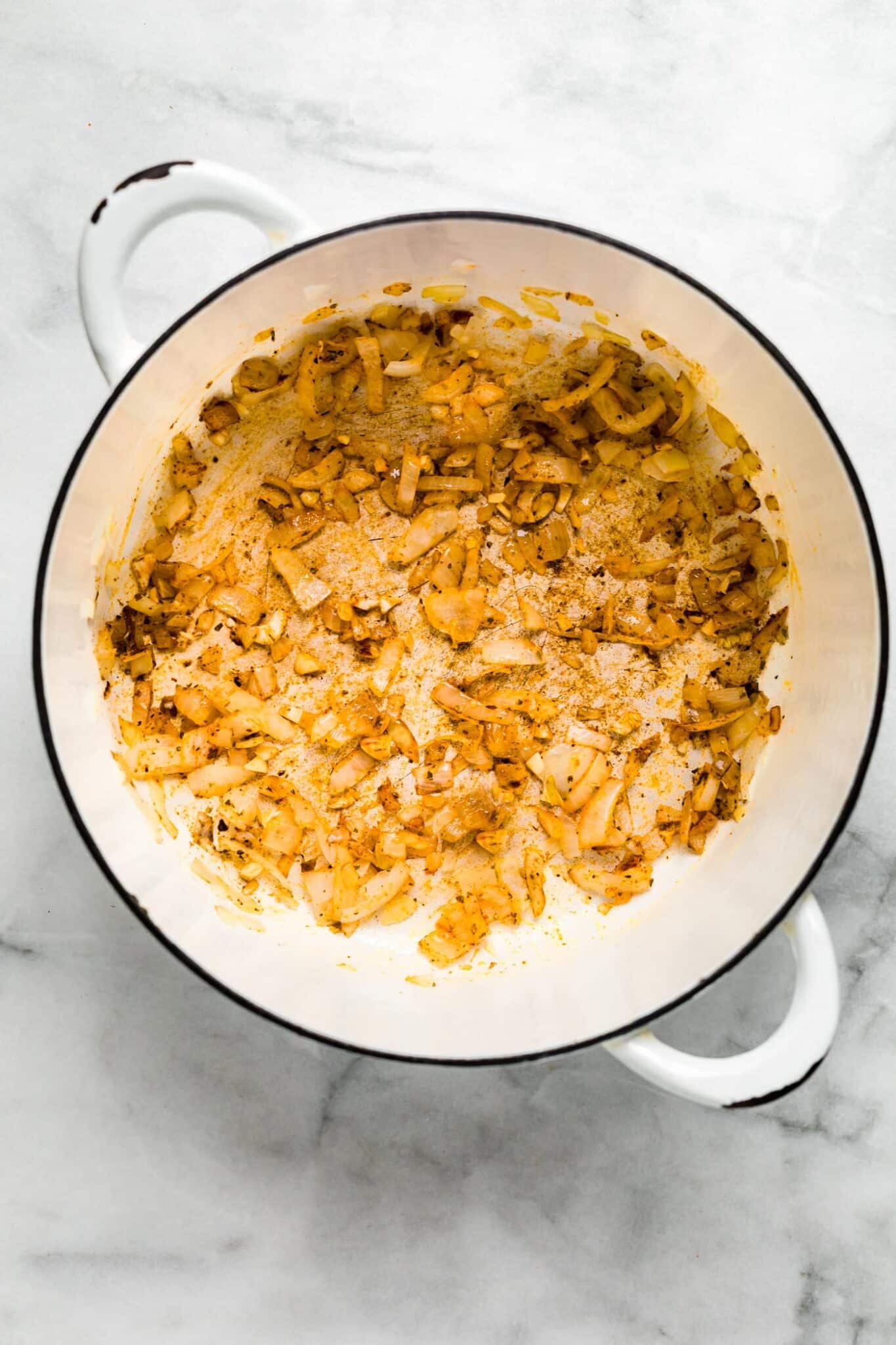 Overhead photo of sauteed onions and garlic in a white soup pot.