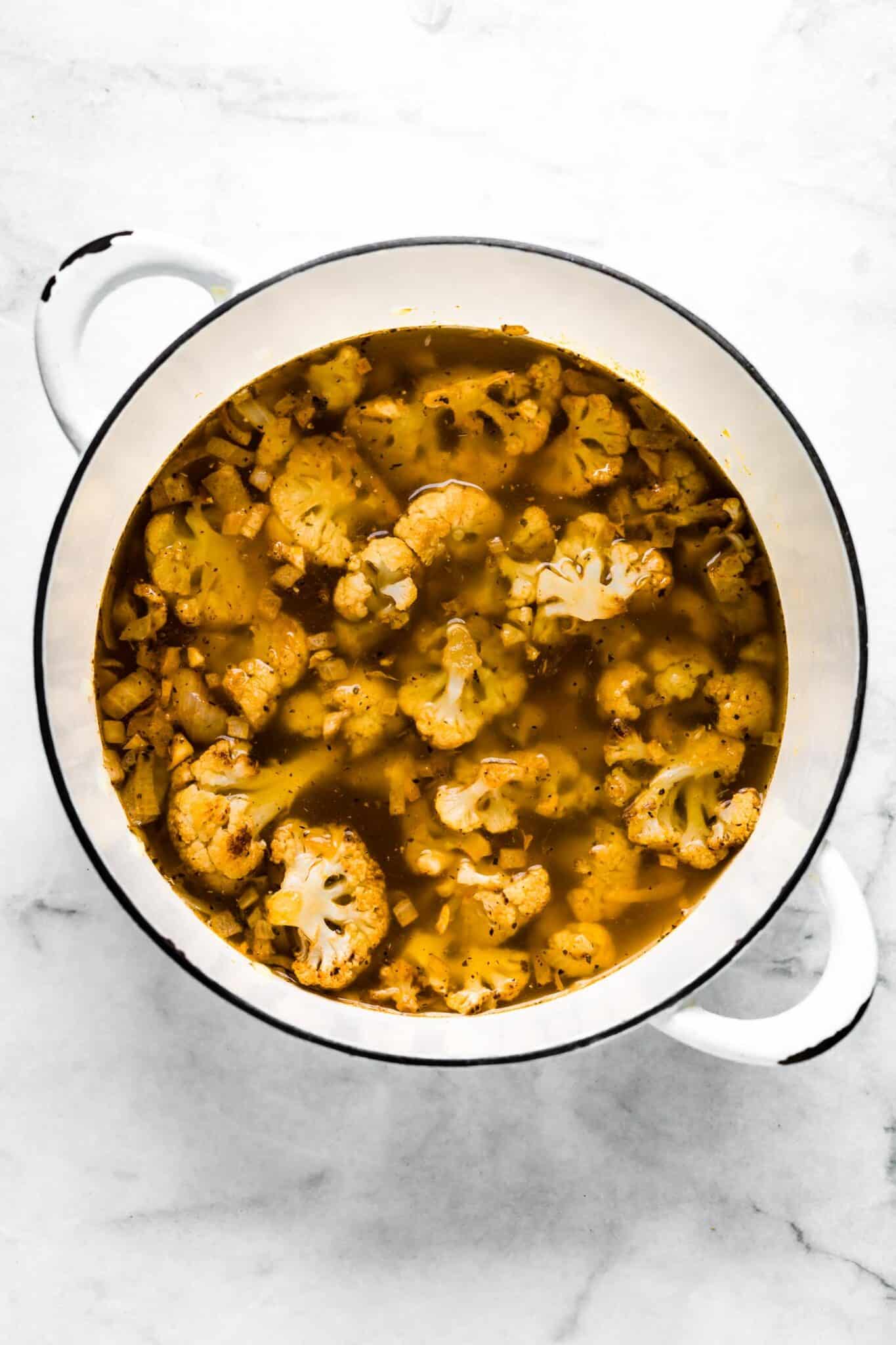 Vegetable broth in a soup pot with roasted cauliflower.
