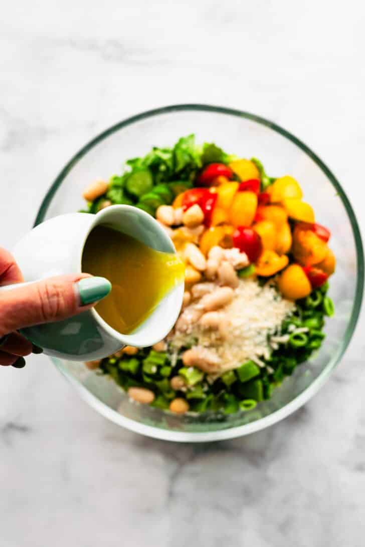 Woman pouring dressing into a bowl of chopped romaine lettuce topped with veggies and beans.