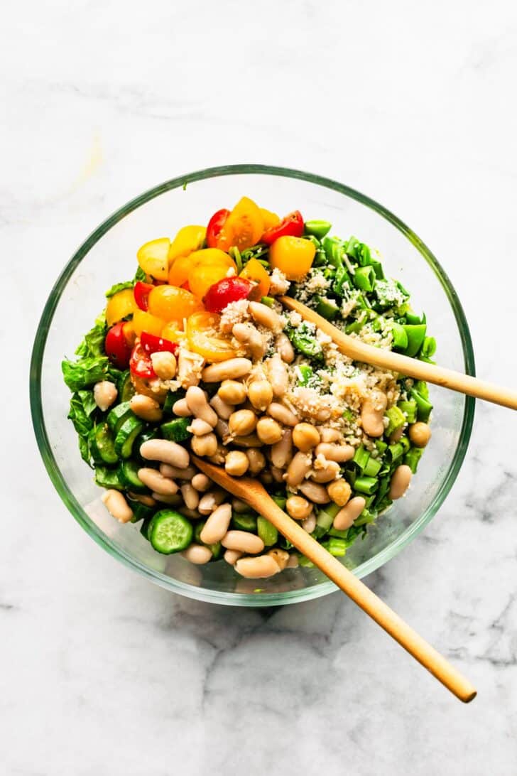 Bowl of romaine salad with white beans, with wooden salad spoons tucked into the greens.