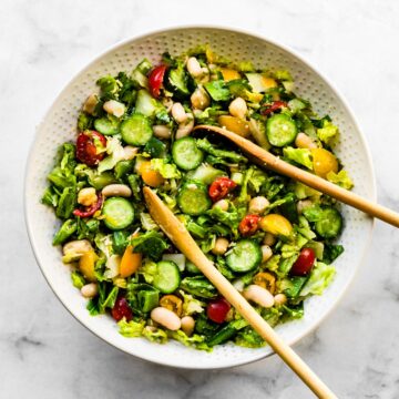 white bowl filled with chopped romaine salad with wood serving spoons in it.