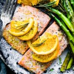 Overhead view two rosemary citrus baked salmon filets on stone plate.