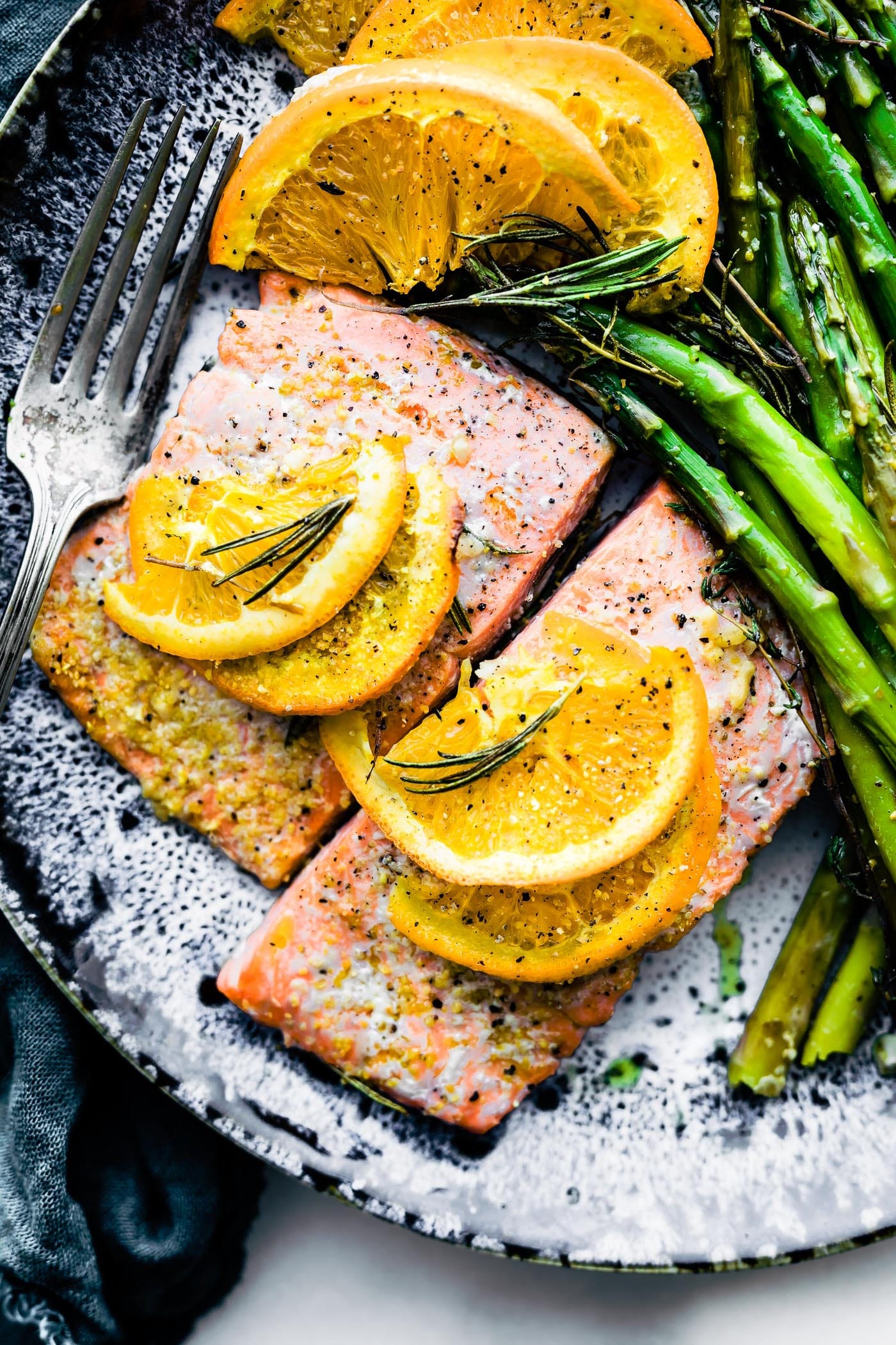 salmon on blue plate with orange slices on top and herbs. overhead angles shot