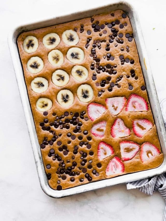 Overhead view of chocolate protein pancakes baked in a baking sheet with four different toppings quartered off in sections.
